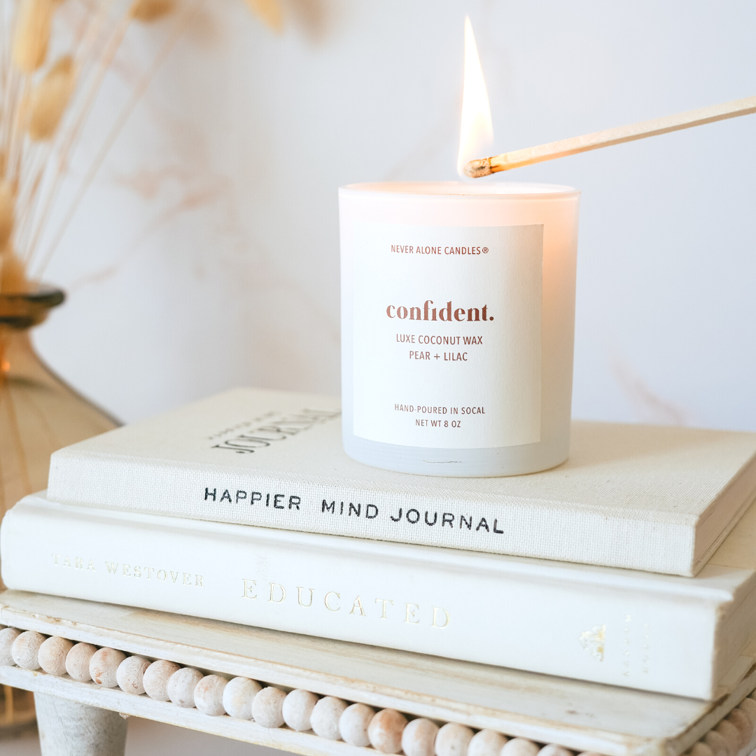 Hand-poured coconut wax candle with a crackling wood wick, scented with brandied pear and French lilac, next neutral colored books.