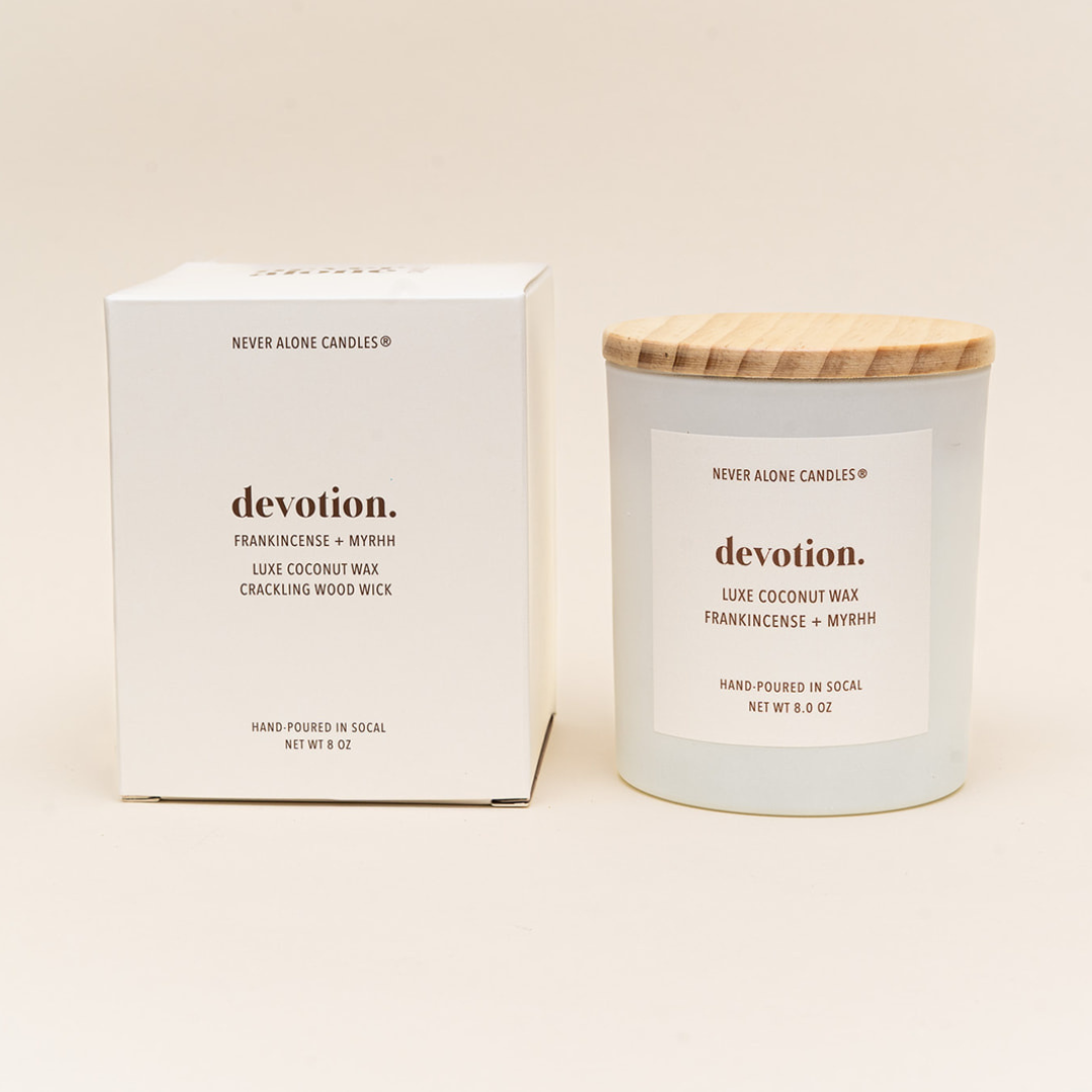 Hand-poured coconut wax candle with a crackling wood wick, scented with frankincense and myrrh, next to a white box with the message about devotion to self care