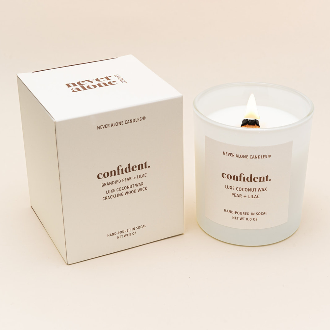 Hand-poured coconut wax candle with a crackling wood wick, scented with brandied pear and French lilac, next to a white box with the message &#39;confident&#39;&#39;
